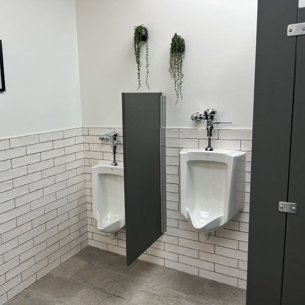 Commercial plumbing installation by JM Lapp displaying a modern men's bathroom with two urinals and a stall.